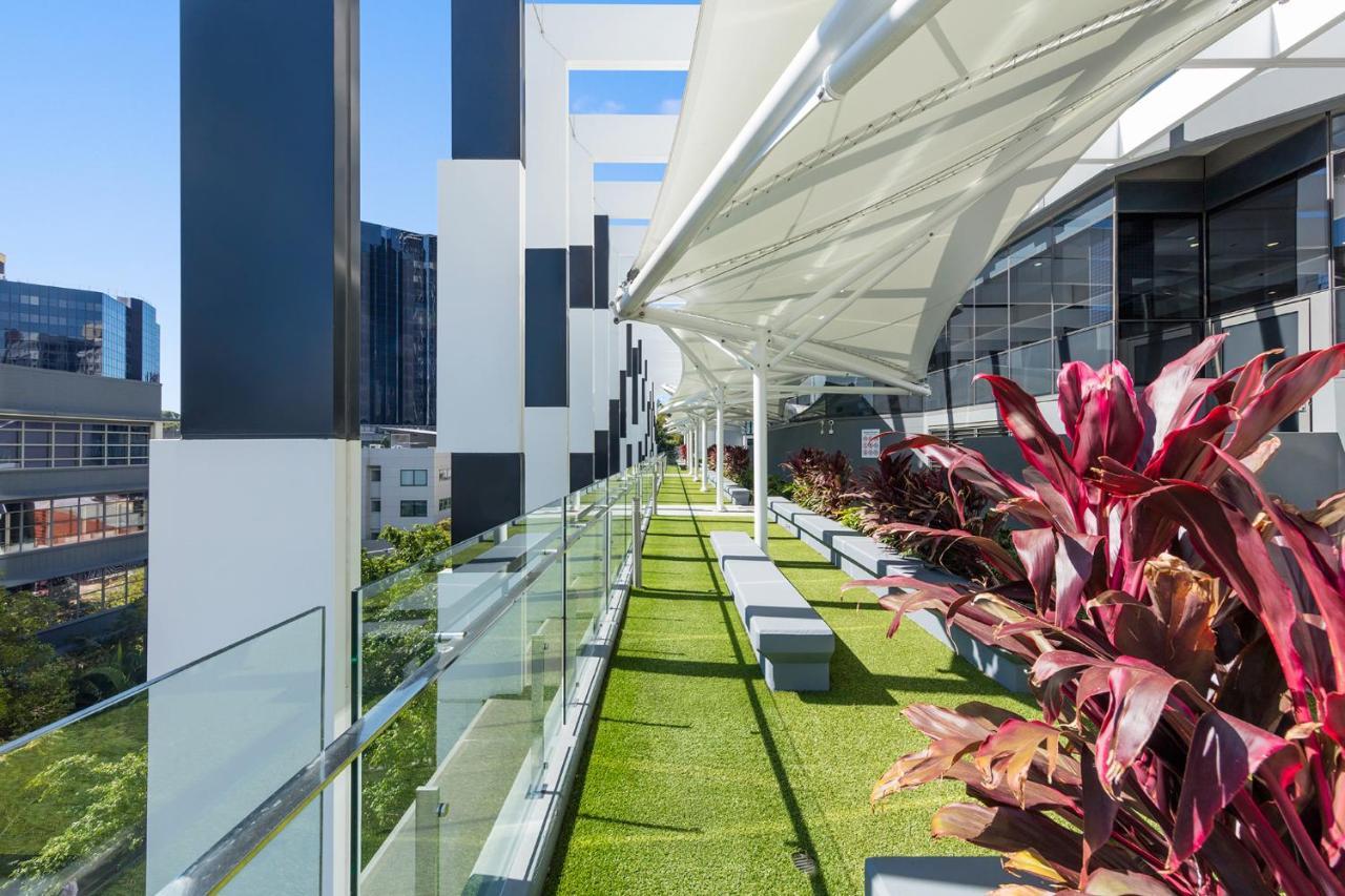 赫歇尔街美利通套房酒店 布里斯班 外观 照片 The photo shows a modern outdoor terrace or balcony area featuring a green lawn-like surface. There are multiple planters with vibrant plants, adding a touch of color. The space has a sleek, contemporary design, with large glass panels providing safe