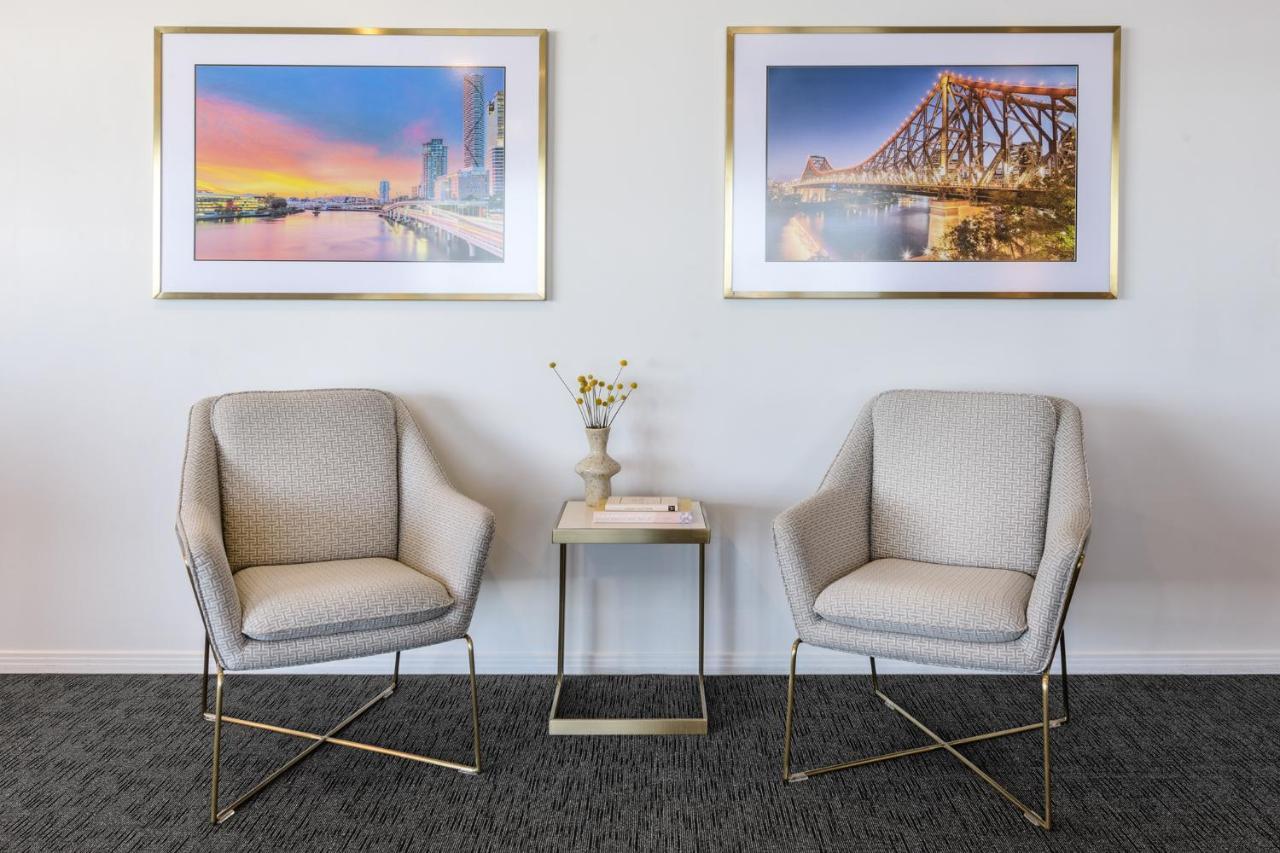 赫歇尔街美利通套房酒店 布里斯班 外观 照片 The photo shows a stylish interior space featuring two modern chairs situated opposite each other. The chairs have a light fabric and a gold metal frame. Between them, there is a small, minimalist side table with a vase containing flowers and a decor