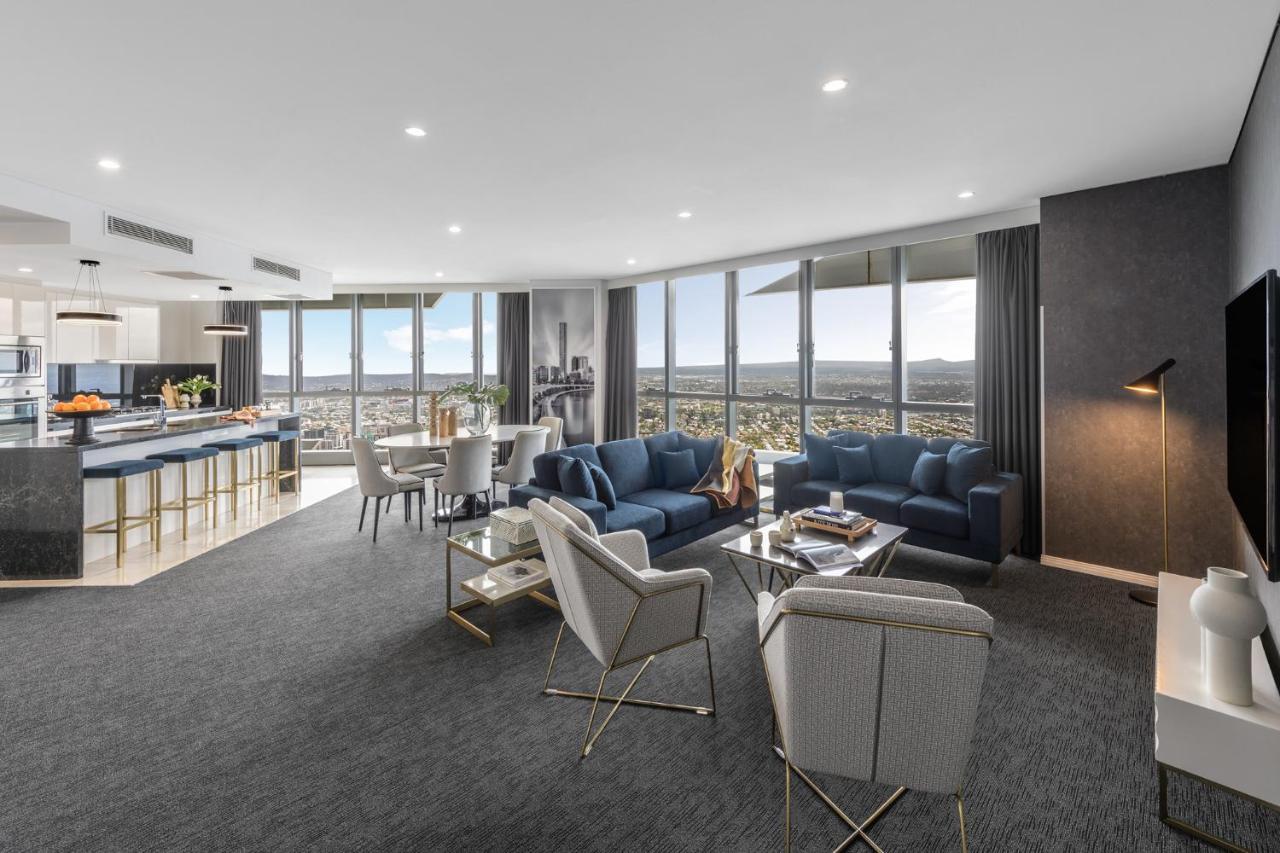 赫歇尔街美利通套房酒店 布里斯班 外观 照片 The photo depicts a modern and stylish living area within a high-rise apartment. The space features large windows that offer a panoramic view of the cityscape. 

1. **Seating Area**: There are two blue sofas and several light-colored chairs arranged 