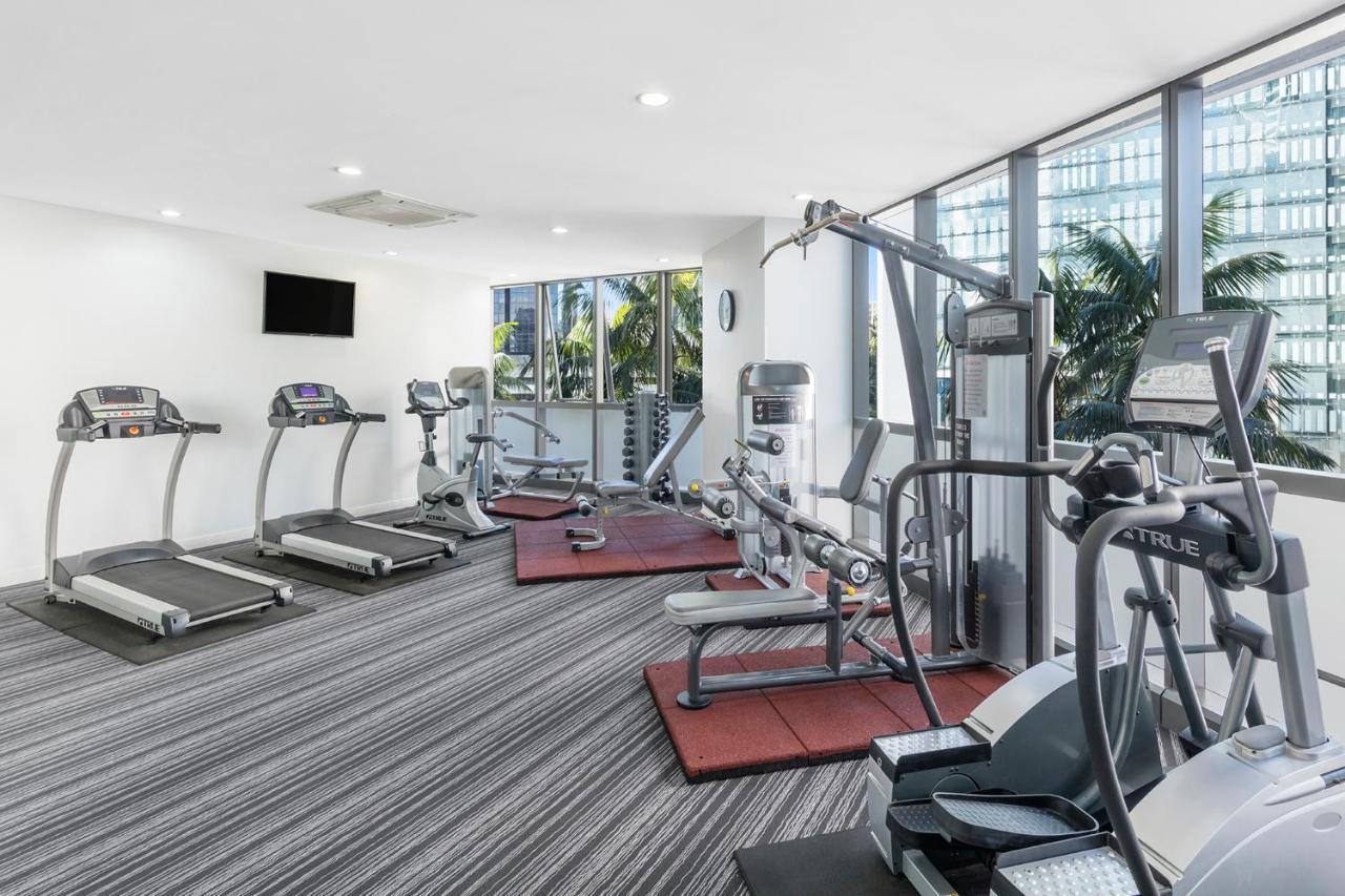 赫歇尔街美利通套房酒店 布里斯班 外观 照片 The photo shows a modern gym or fitness area that features several exercise machines. There are multiple treadmills lined up against one wall, all facing a large window that lets in natural light and offers a view of greenery outside. In the center, 