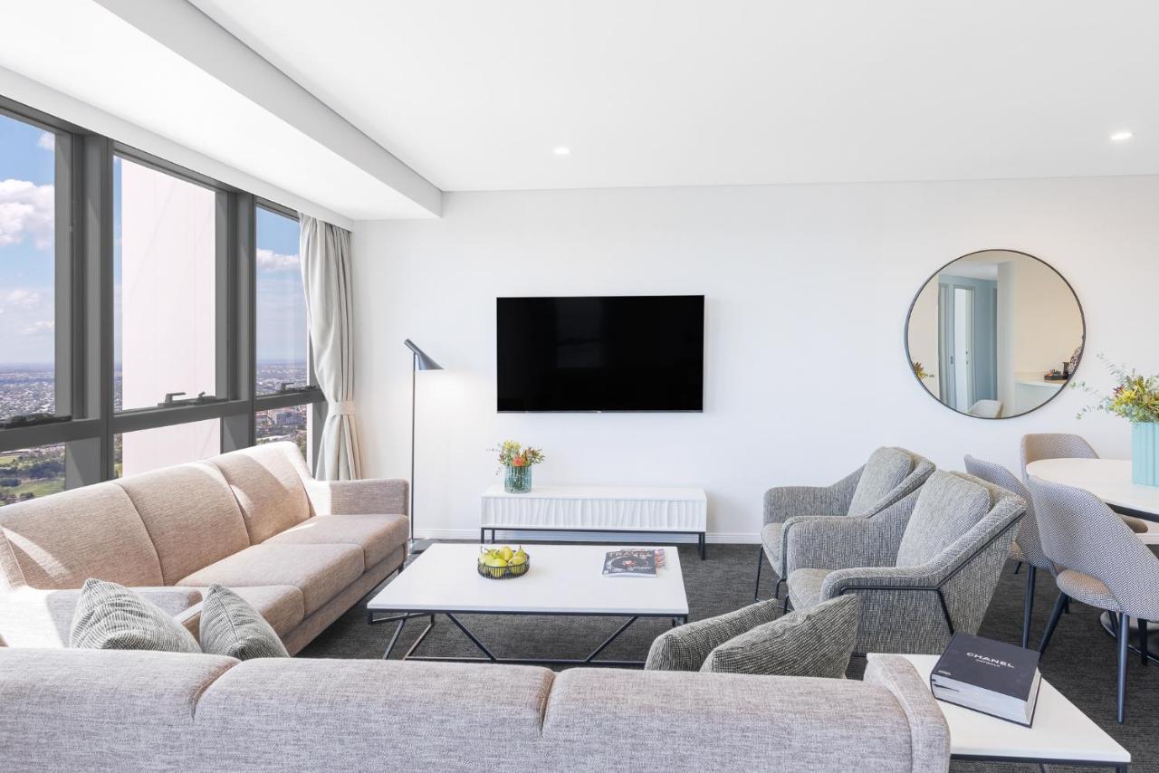 赫歇尔街美利通套房酒店 布里斯班 外观 照片 The photo shows a modern living room with a bright and spacious atmosphere. It features a light-colored couch and two grey armchairs arranged around a coffee table. A flat-screen television is mounted on the wall, and there is a round mirror nearby, 