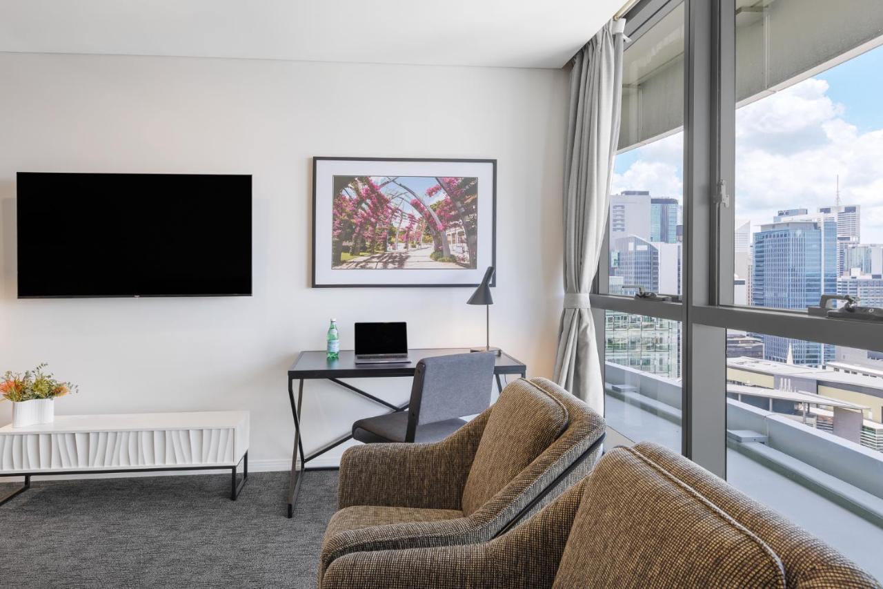 赫歇尔街美利通套房酒店 布里斯班 外观 照片 The photo shows a modern room interior that includes two comfortable chairs with a textured fabric, a television mounted on the wall, and a desk featuring a laptop and a lamp. A piece of artwork is displayed on the wall above the desk. Large windows 